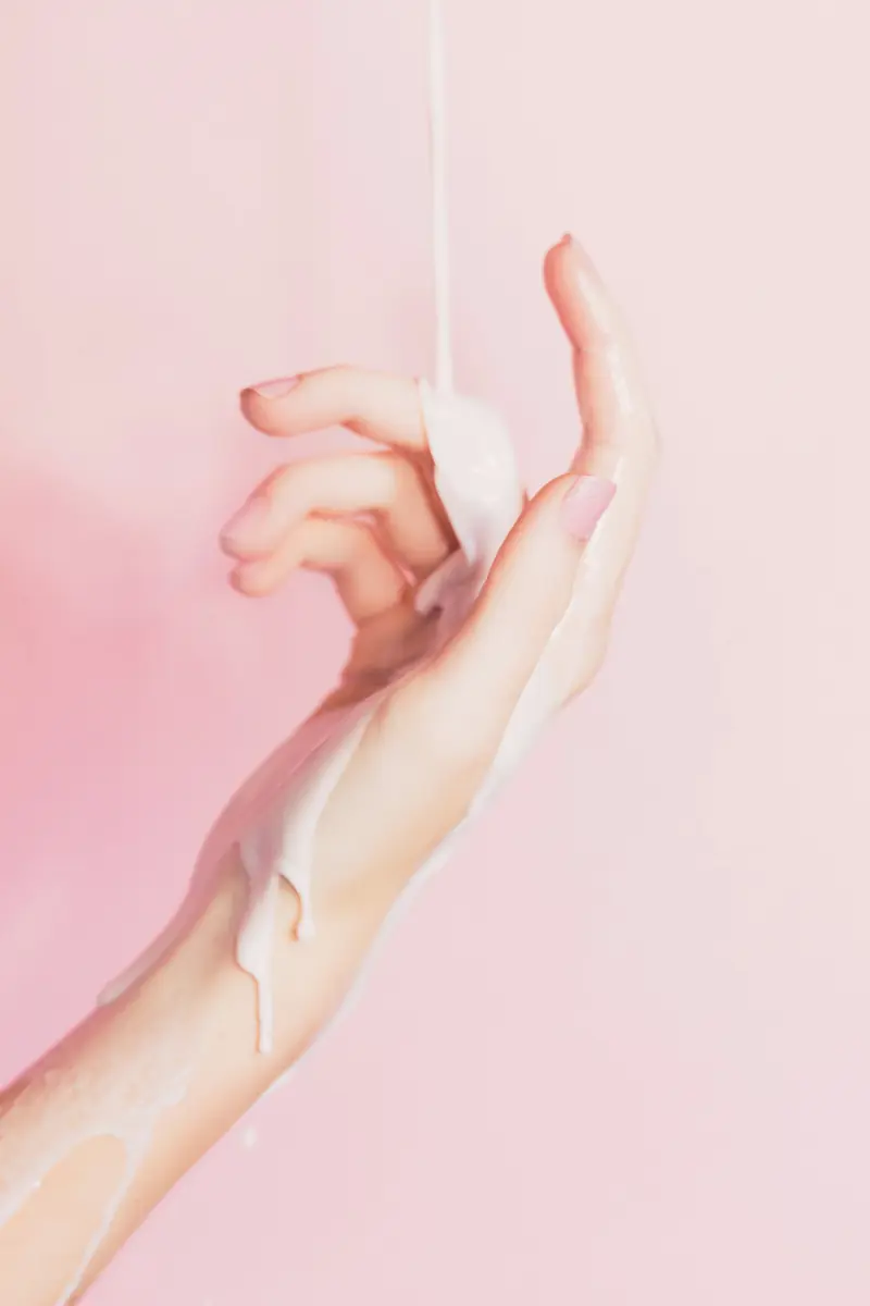 Mano con crema hidratante sobre un fondo rosa